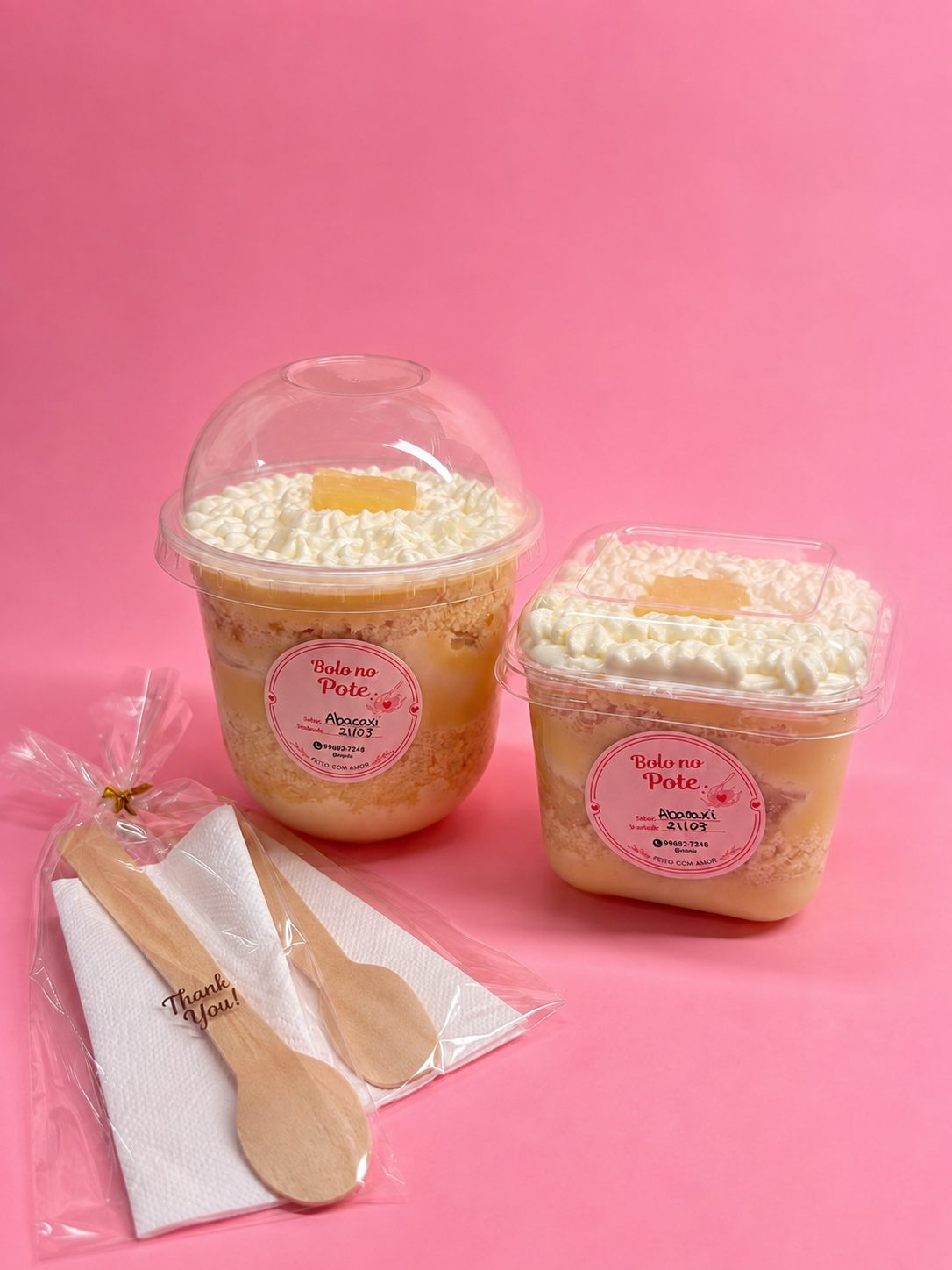 Dois potes de bolo de abacaxi com coco, acompanhados de colheres embaladas